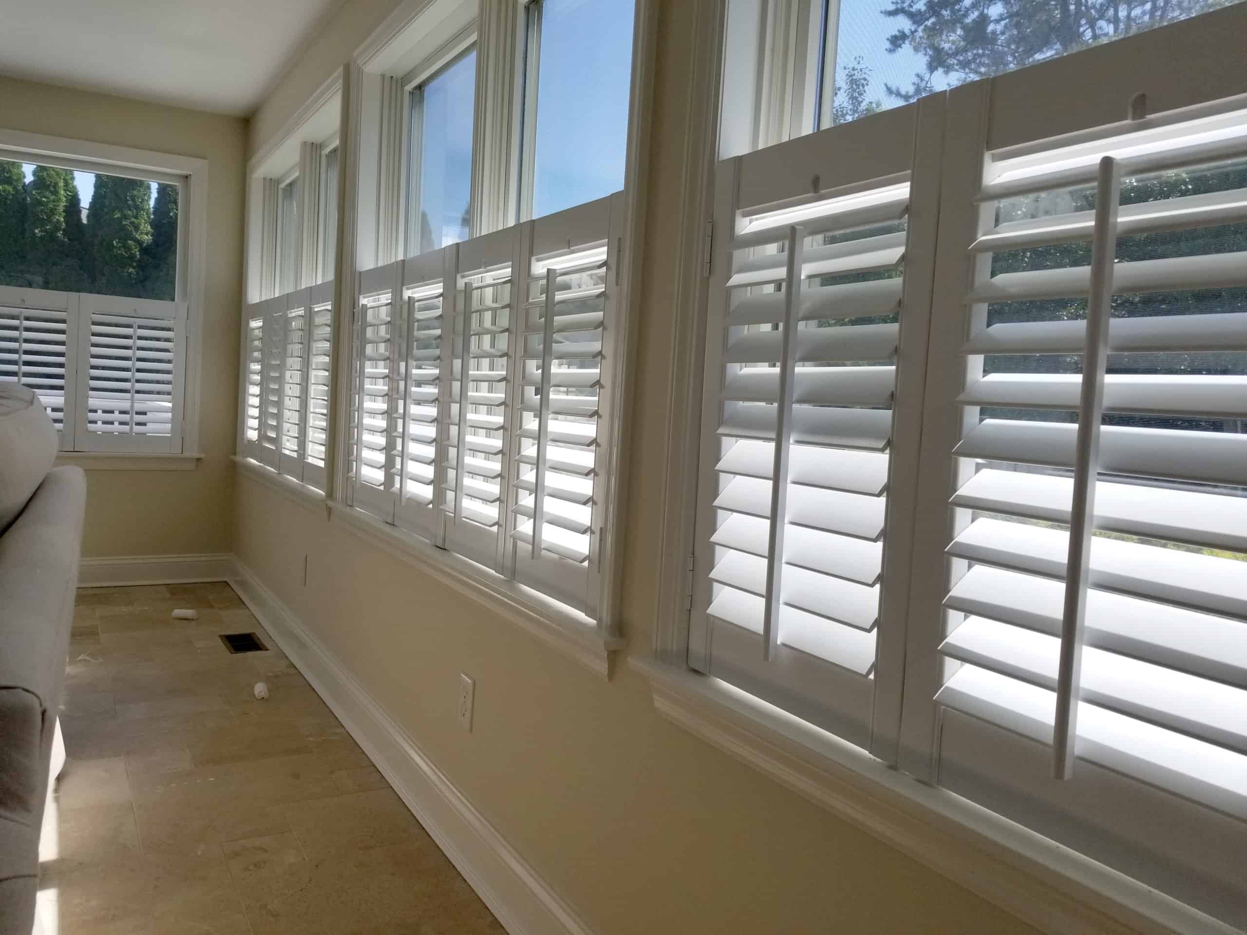 A row of large windows fitted with white plantation shutters partially opened to let in natural light.