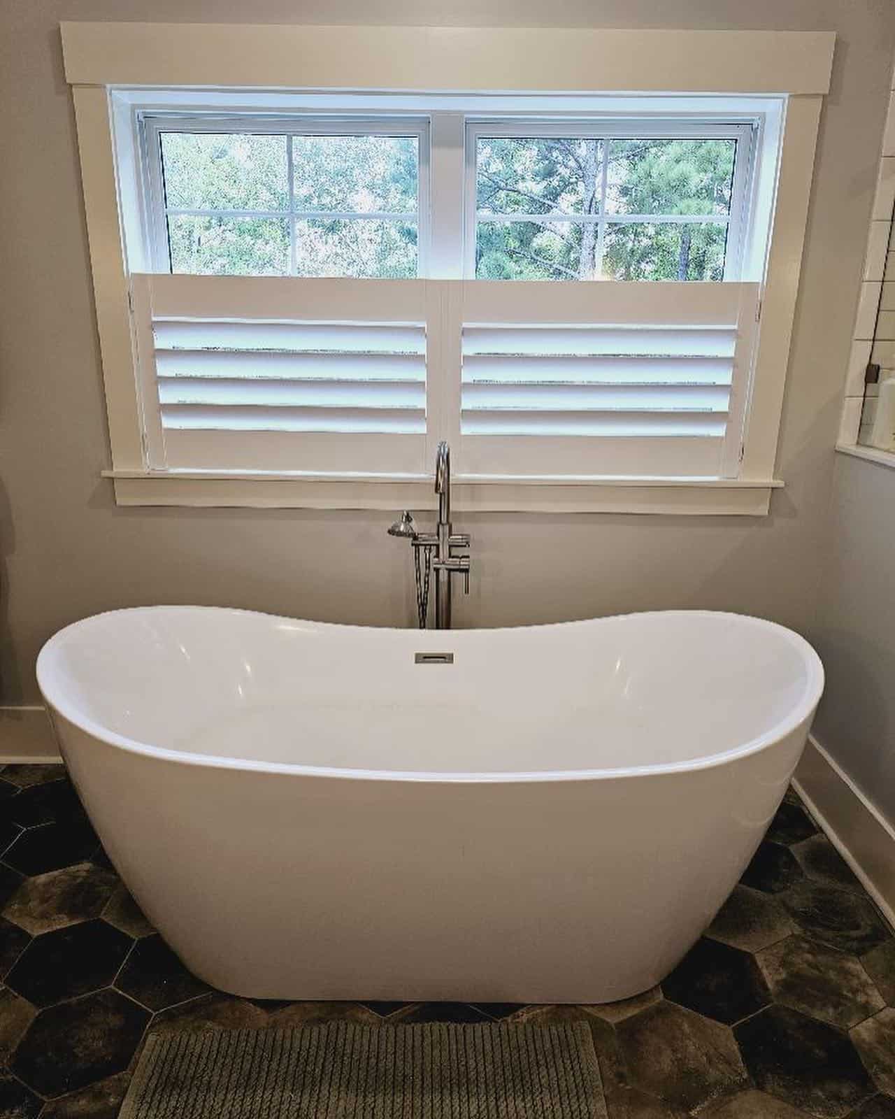 Freestanding bathtub with window shutters in a modern bathroom setting.
