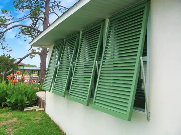 Partly open green louvered hurricane shutters reveal North Carolina style window treatments charm.