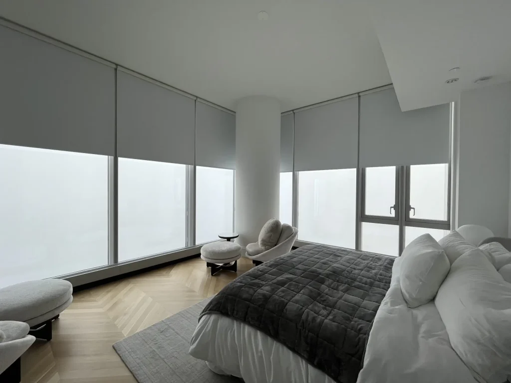 Modern bedroom in North Carolina with large windows, grey bedding, two chairs, and custom window treatments.
