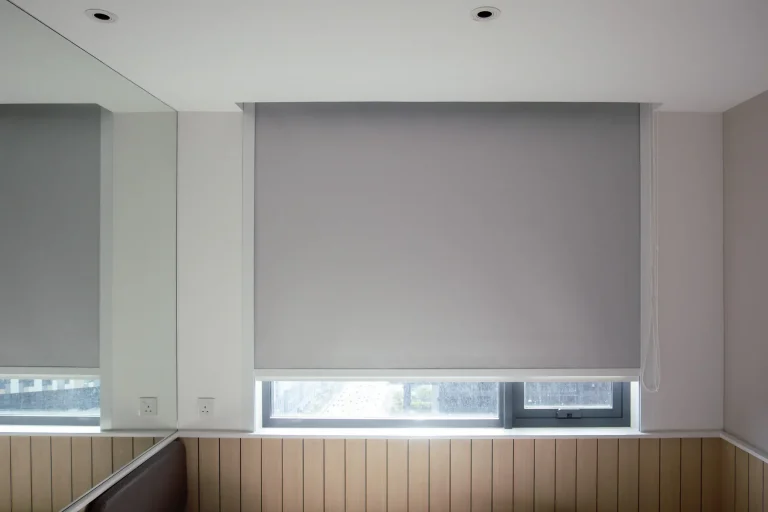 A gray roller blind from Window Treatments North Carolina covers a window in a stylish paneled room.