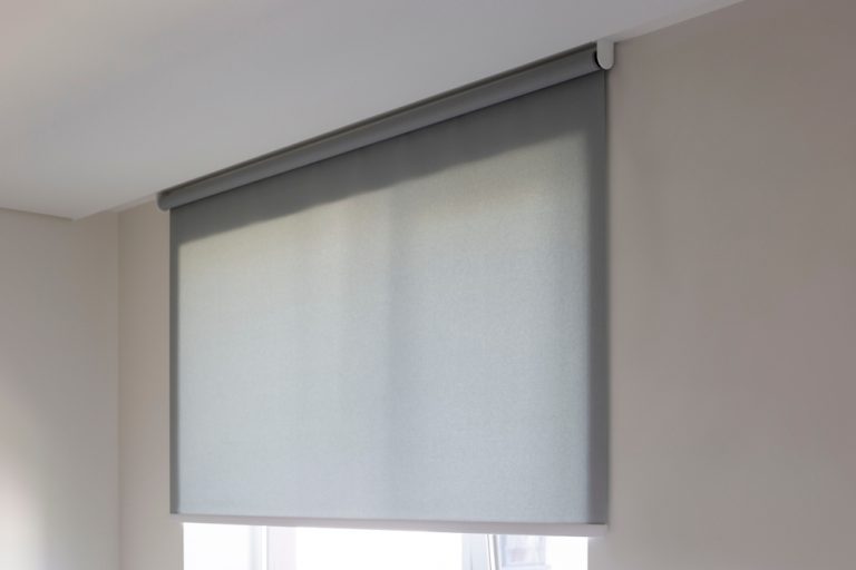A closed grey roller blind from Window Treatments North Carolina covers a window on a pale wall.